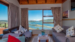 Habitación con un ventanal grande que ofrece una vista panorámica del paisaje costero, amoblada con sofá, sillón y una mesita con una planta.
