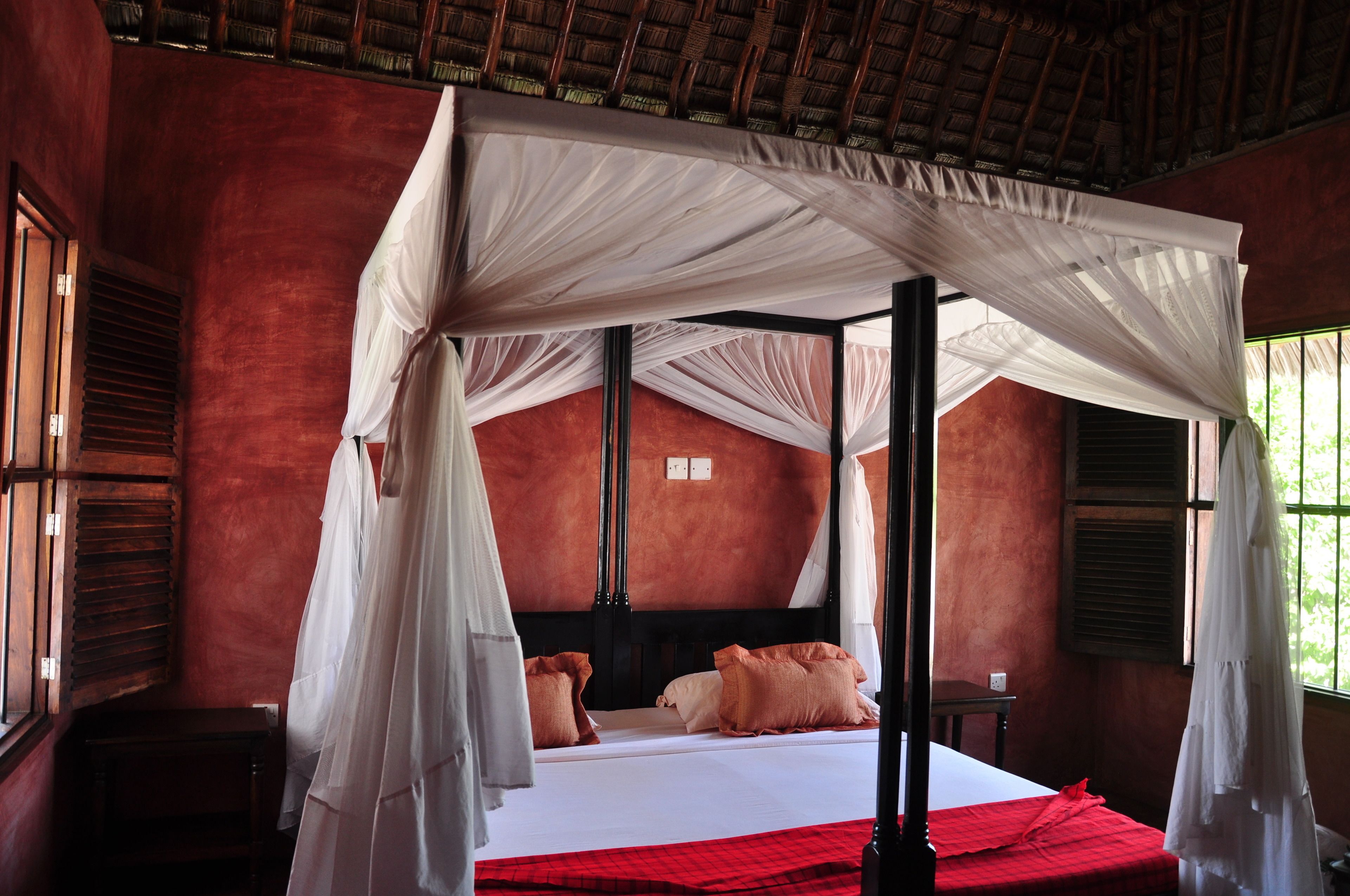 A room with a four-poster bed, red bedding, and a canopy.