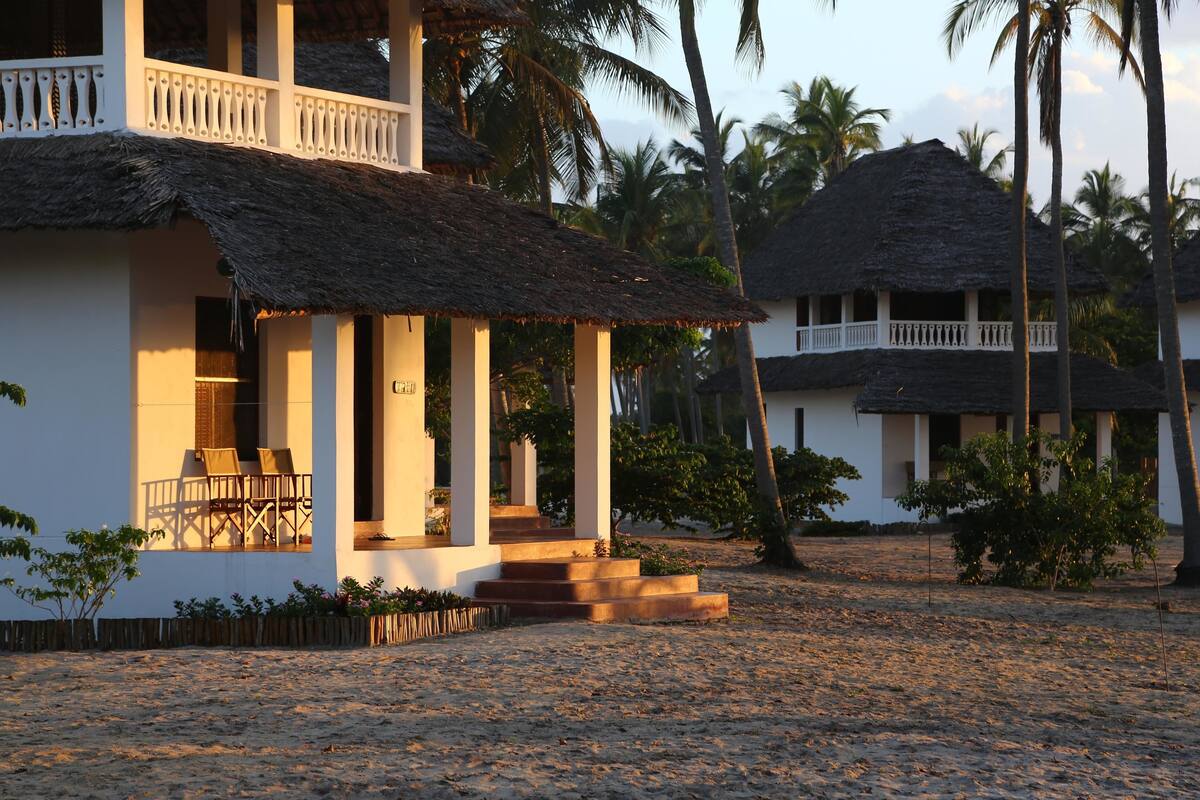 A two-story building with a thatched roof, a balcony, and a staircase leading to the entrance.