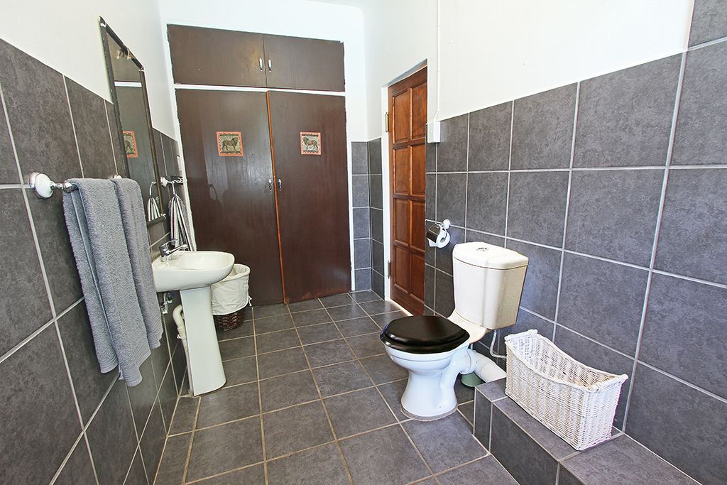 A bathroom with a toilet, sink, and a mirror. There are towels hanging on the wall and a basket on the floor.