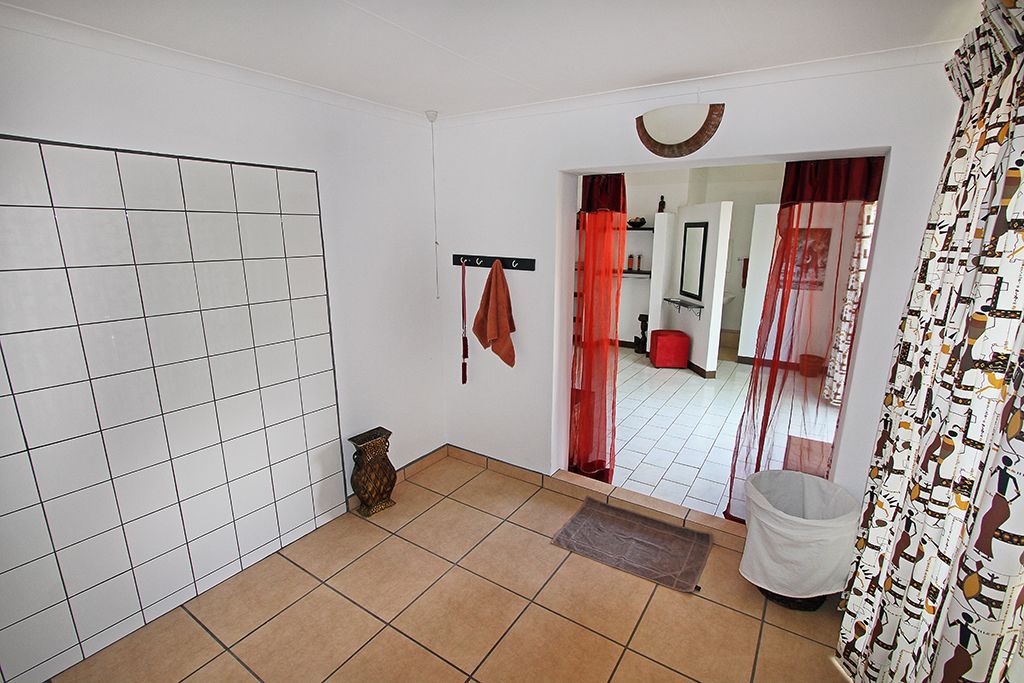 A bathroom with white tiled walls, a tiled floor, a towel rack with a towel, a trash bin, and a shower area with a curtain.