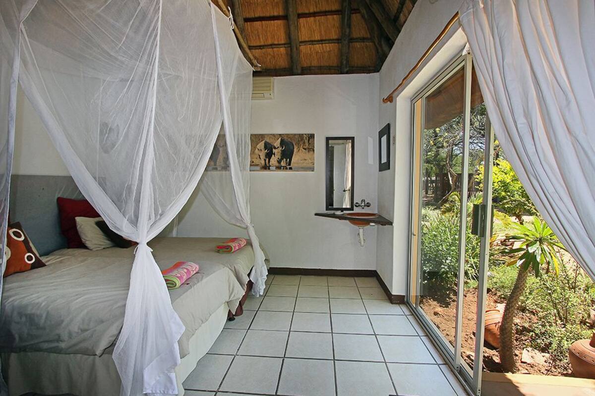 Un dormitorio con una cama bajo una mosquitera, un lavamanos pequeño y vistas al exterior.