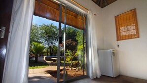 Una habitación con puerta corrediza de vidrio que da a un jardín, un refrigerador y una persiana enrollable en la pared.