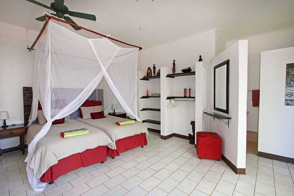 Un dormitorio con una cama con dosel, un ventilador de techo y un taburete pequeño rojo.