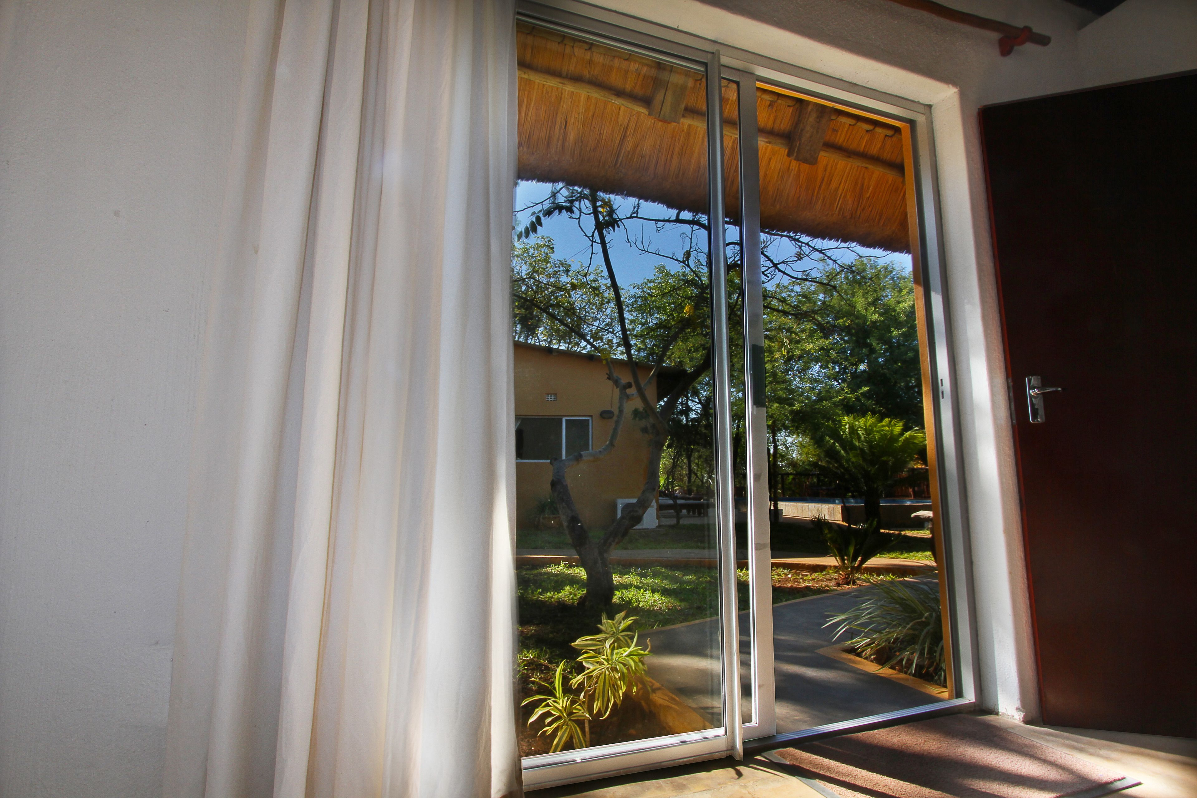 A sliding glass door with a view of a residential area, including a house and trees.