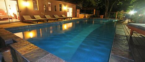A swimming pool with lounge chairs and a building with a glass door.