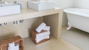 A bathroom with a sink, a bathtub, and two wicker baskets containing towels and toilet paper.