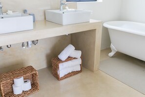 A bathroom with a sink, a bathtub, and two wicker baskets containing towels and toilet paper. - 401 Rozendal Cottages (Stellenbosch)