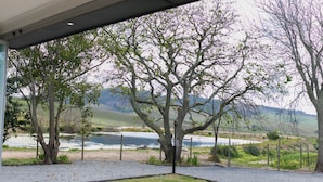 A view from a covered outdoor area with a gravel path leading to a lake, surrounded by trees and a fence. - 401 Rozendal Cottages (Stellenbosch)