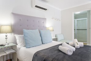 A hotel room with a large bed, two bedside tables with lamps, a glass shower enclosure, and a view of the outside. - 401 Rozendal Cottages (Stellenbosch)