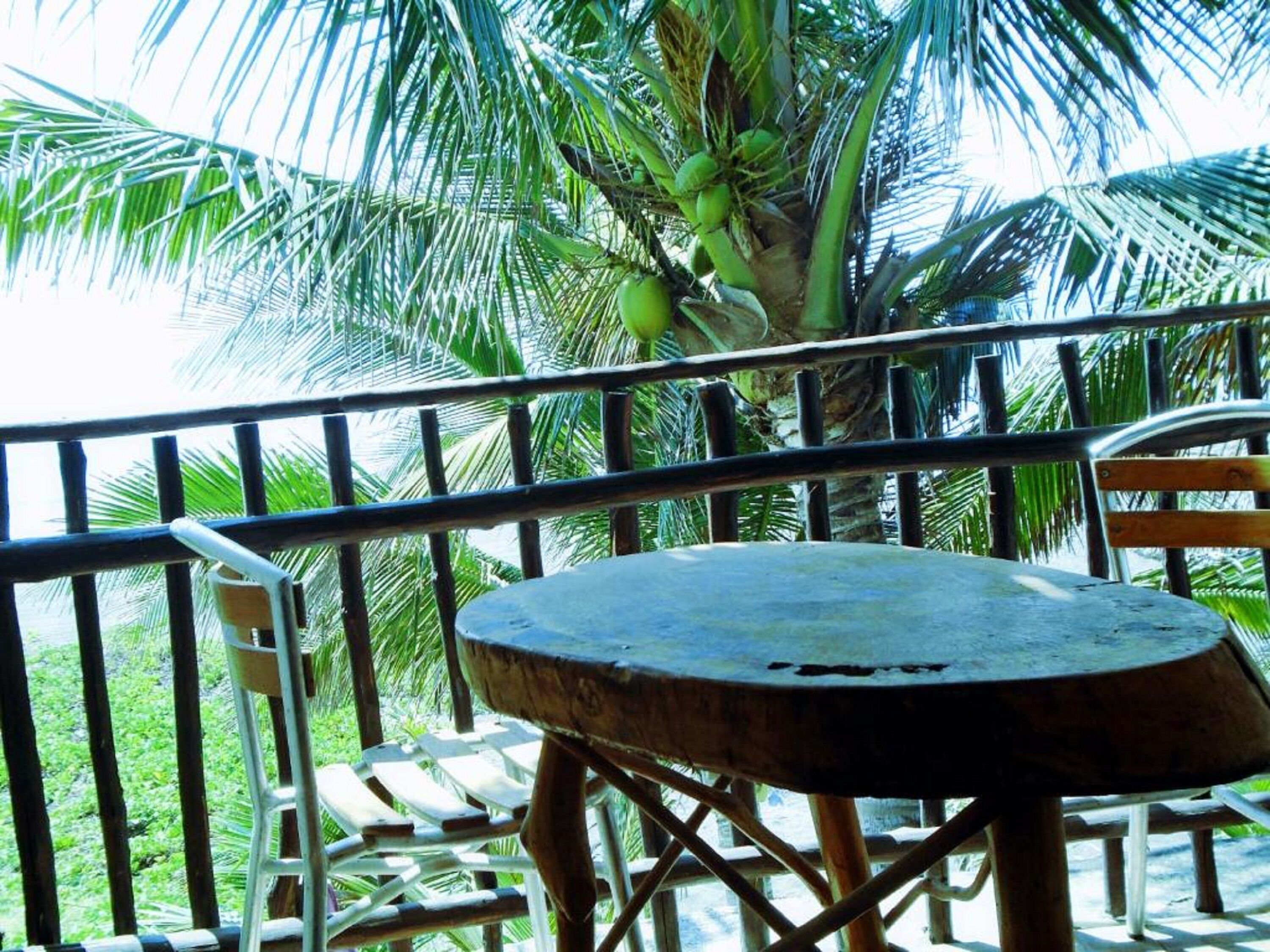 A round table with a metal frame, surrounded by white plastic chairs, on a balcony with a metal railing.