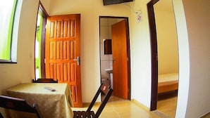 A room with a wooden door, a small table with a tablecloth, a chair, a television mounted on the wall, and a tiled floor. - Pousada Montanhas do Bem TeVi (Caraguatatuba)