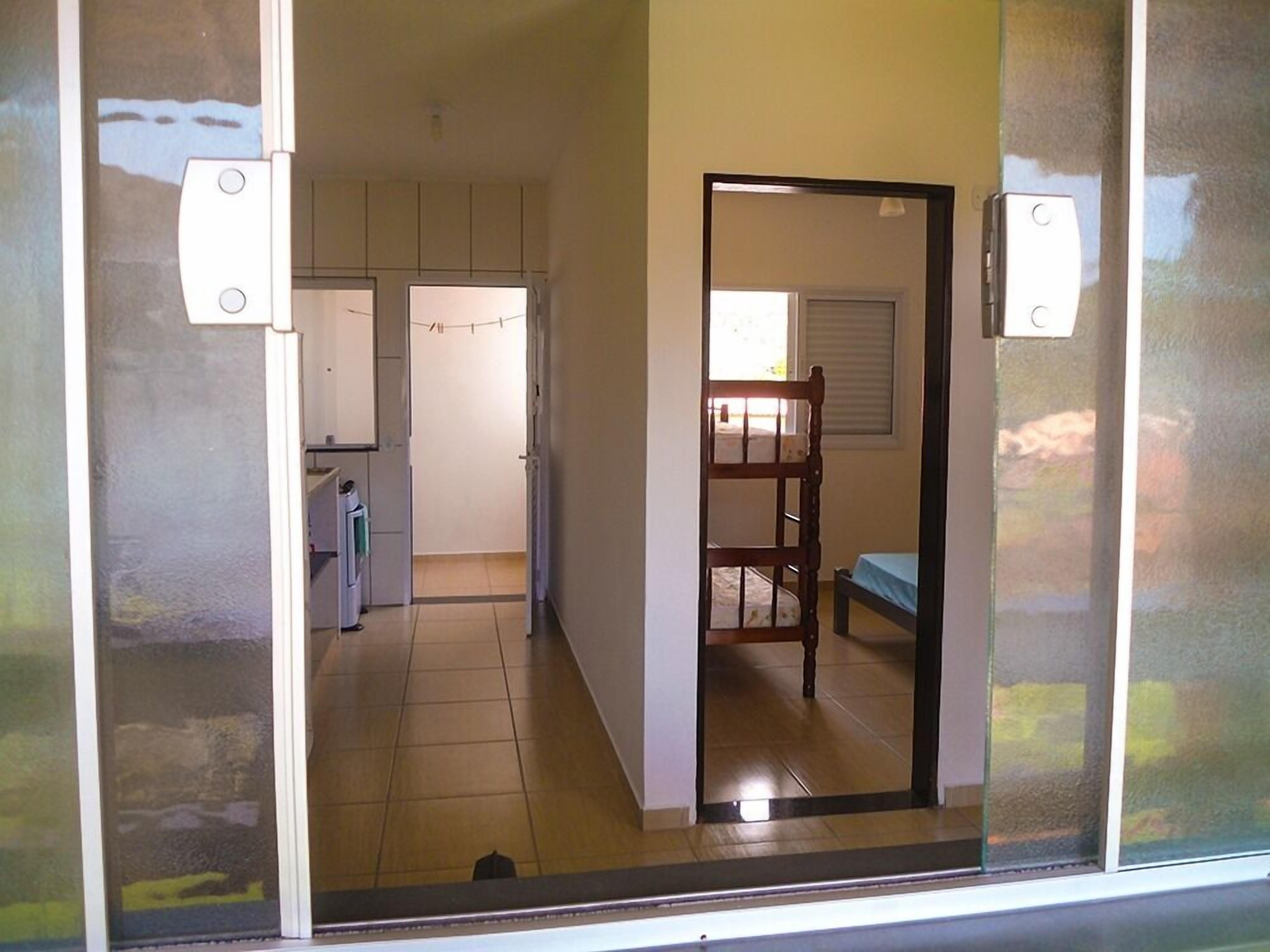 Ein Zimmer mit einem Bett, einem Stuhl und einem Fenster. Eine Tür führt in einen weiteren Raum.