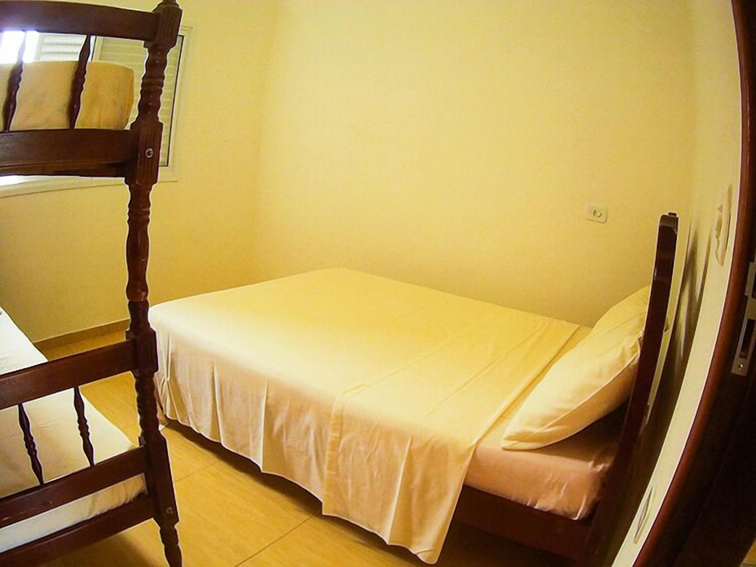 Ein kleines Zimmer mit einem Einzelbett, einem Holz-Kopfteil und einer schlichten weißen Bettdecke.