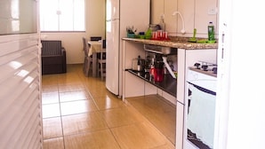 A compact kitchen with a refrigerator, sink, and stove. There is a dining area with a table and chairs. - Pousada Montanhas do Bem TeVi (Caraguatatuba)