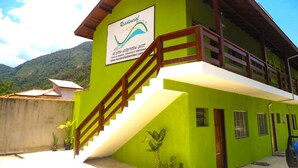 A two-story building with a green facade, a wooden staircase, and a sign indicating it is a residential property. - Pousada Montanhas do Bem TeVi (Caraguatatuba)