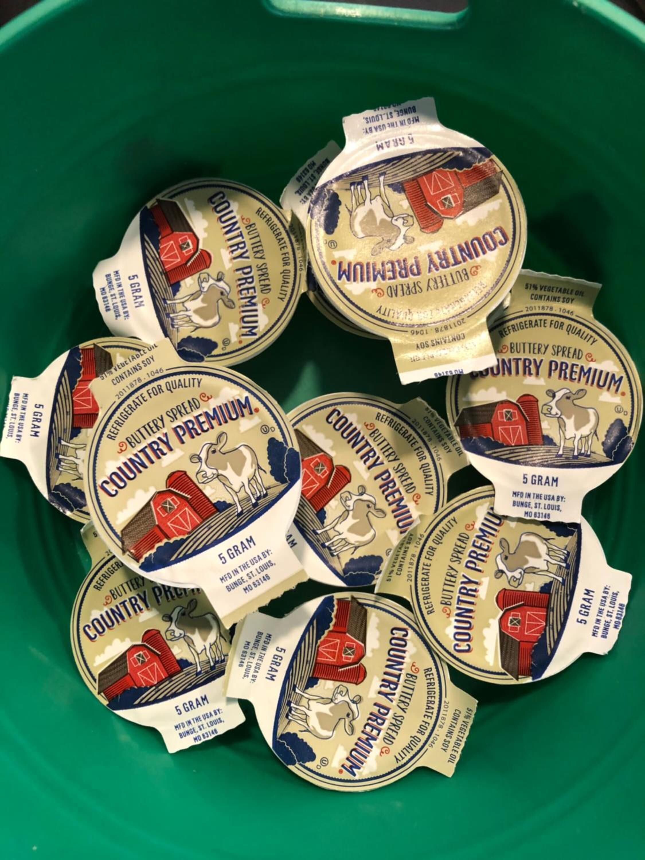 A green container filled with multiple 5-gram Country Premium butter spread packages.