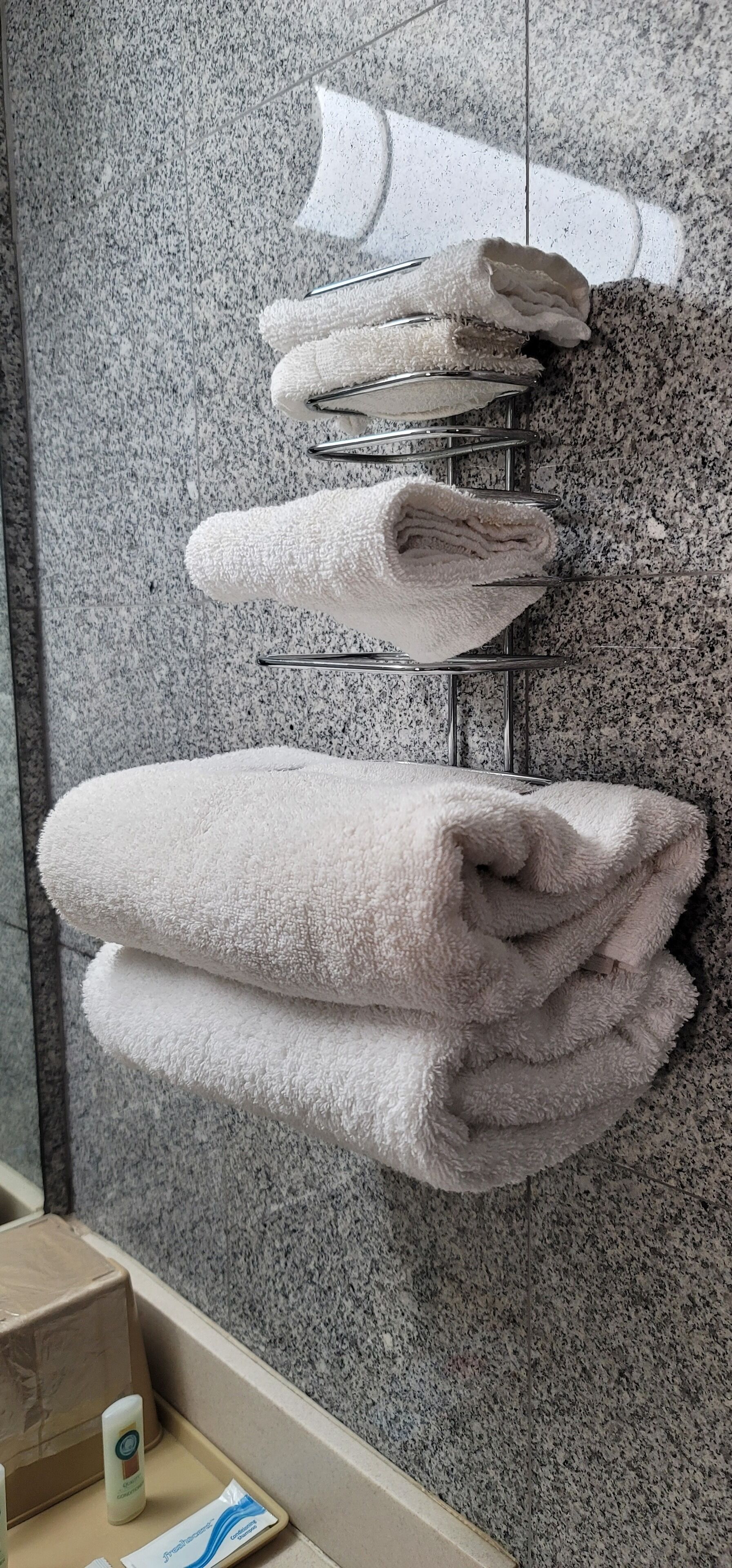 A bathroom with a granite countertop, a towel rack with folded towels, and a small tray with toiletries.