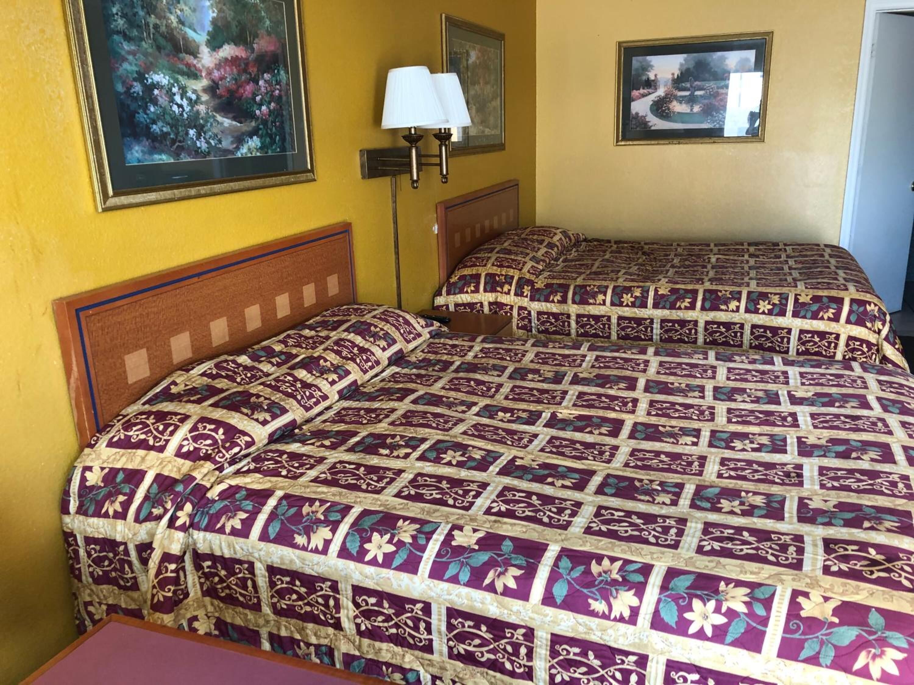 A hotel room with two beds, a nightstand, a lamp, and two framed pictures on the wall.