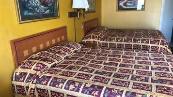 A hotel room with two beds, a nightstand, a lamp, and two framed pictures on the wall.