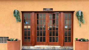 Zona de recepción en el lobby, con una puerta de madera, un botón pulsador y dos plantas en macetas.