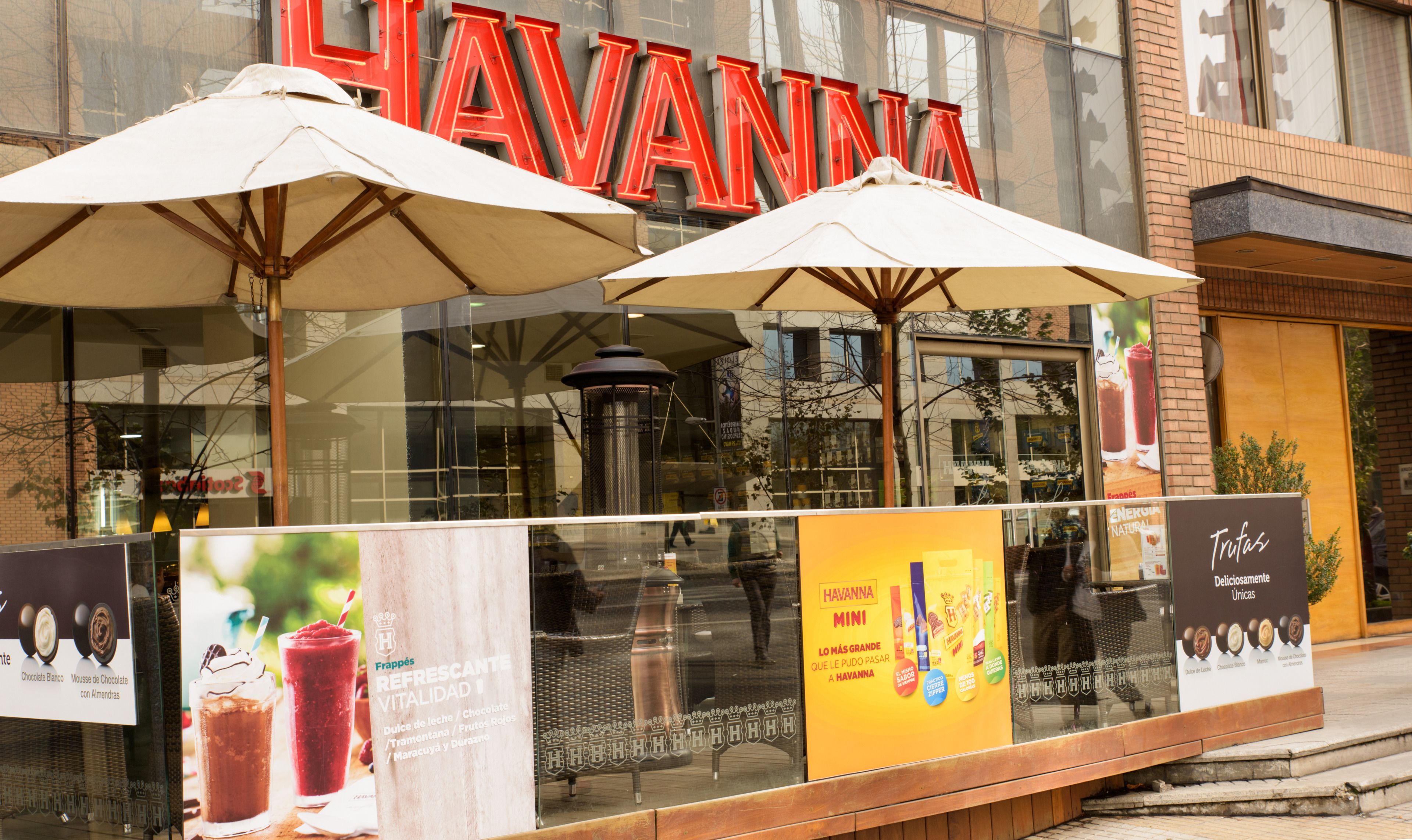 Un escaparate con letras rojas grandes que dicen "HAVANNA" sobre la entrada. Hay dos sombrillas blancas frente a la tienda.