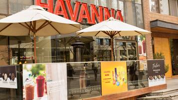 Un escaparate con letras rojas grandes que dicen "HAVANNA" sobre la entrada. Hay dos sombrillas blancas frente a la tienda.