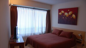 Un cuarto de hotel con una cama grande, un televisor de pantalla plana, una mesita de noche, una lámpara y un cuadro en la pared.
