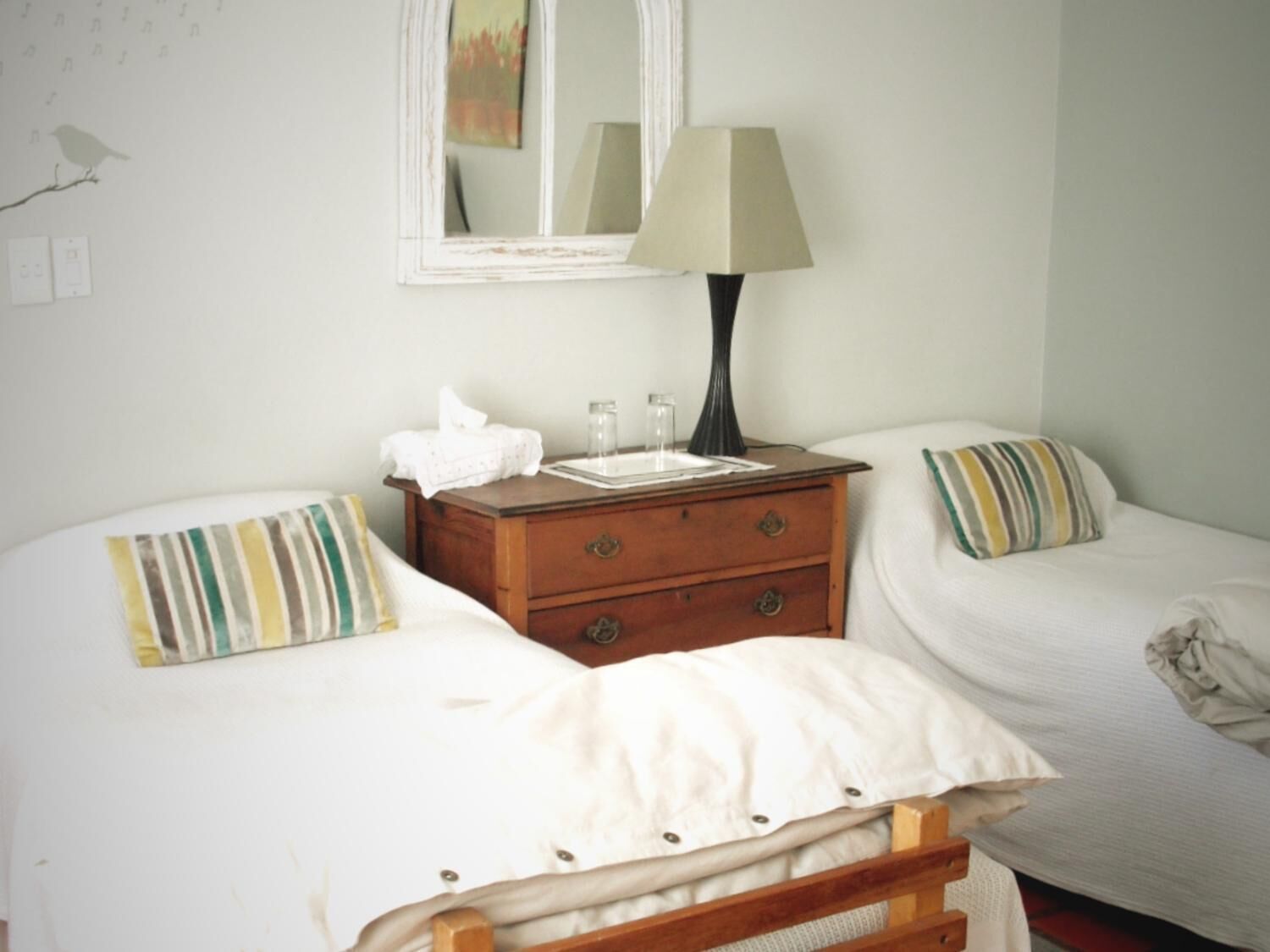 A bedroom with two beds, a nightstand with a lamp, and a mirror on the wall.