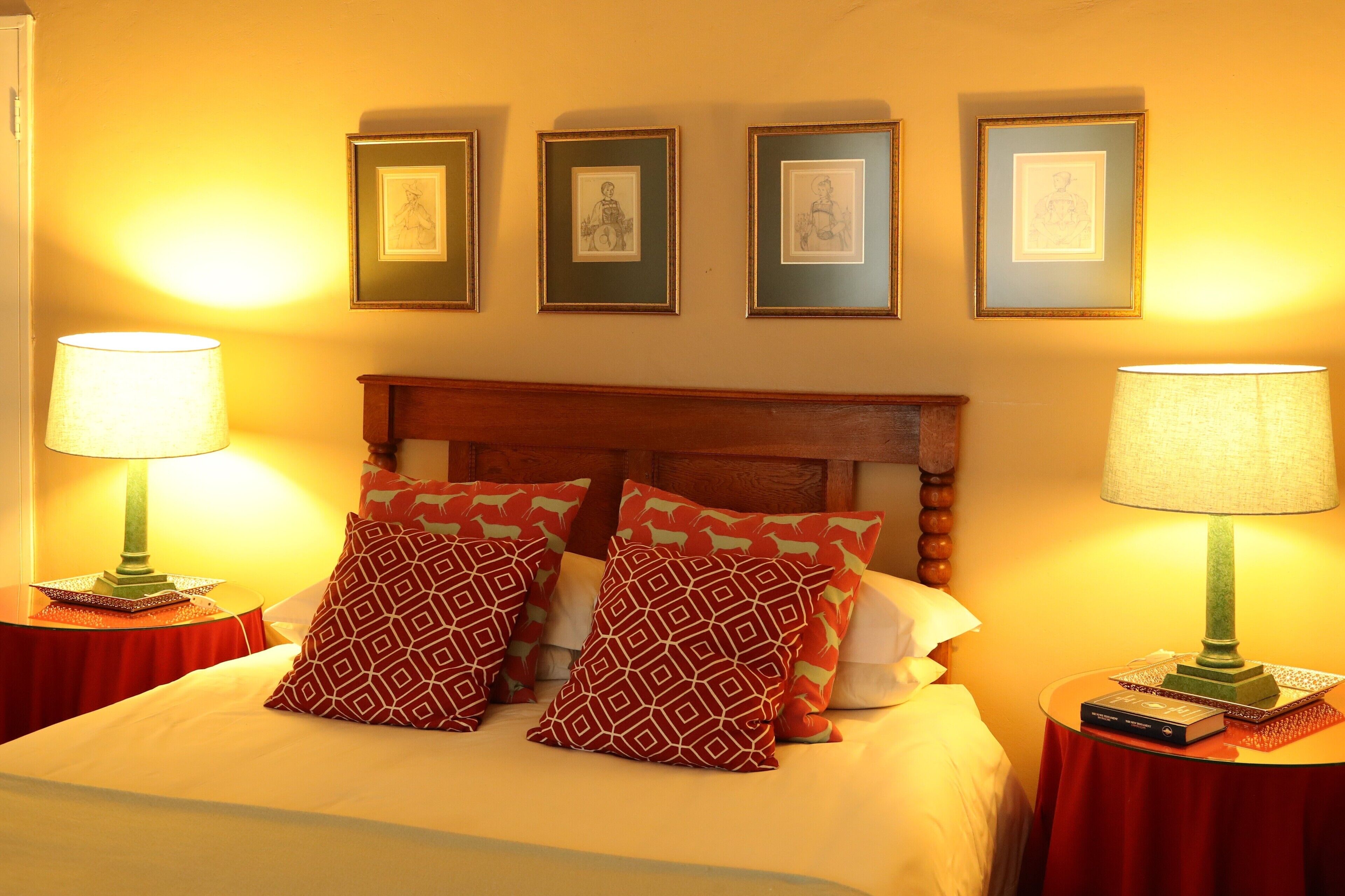 A hotel room with a bed, two nightstands, a wooden headboard, and three framed pictures on the wall.
