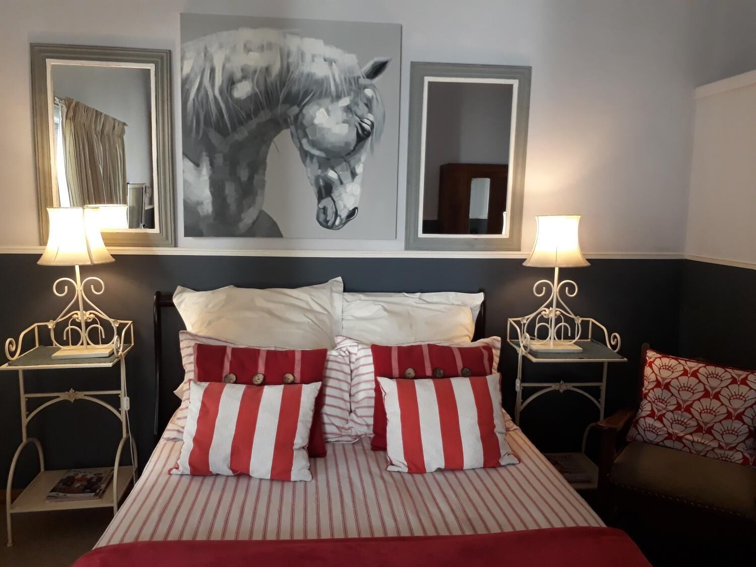 A hotel room with a bed, two bedside tables with lamps, a large framed horse painting, and a mirror.