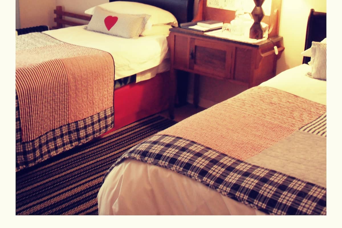 A hotel room with two beds, a nightstand, a lamp, and two framed pictures on the wall.