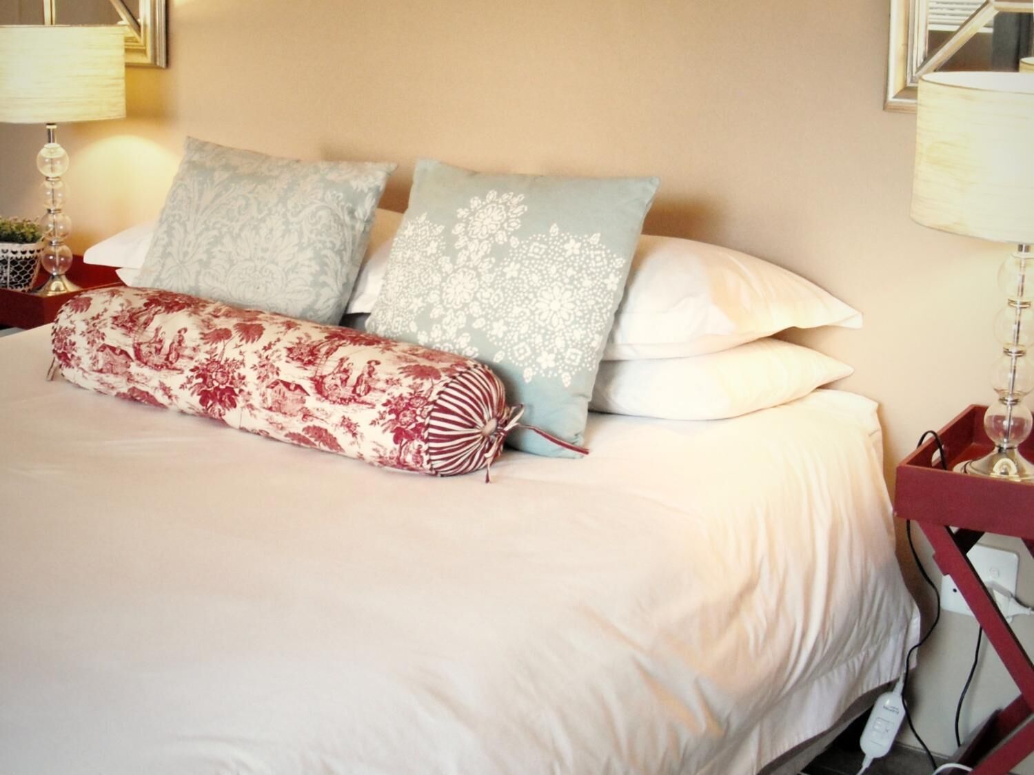 Een net opgemaakt bed met een kussen met bloemenprint en een decoratief cilinderkussen.