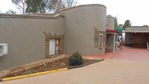A building with a curved facade, a small garden area with plants, and a paved entrance. - Aligeo Guest House (Senqu)