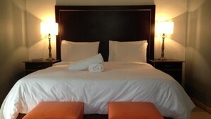 A neatly made bed with white linens, two bedside lamps, and two orange ottomans. - Aligeo Guest House (Senqu)