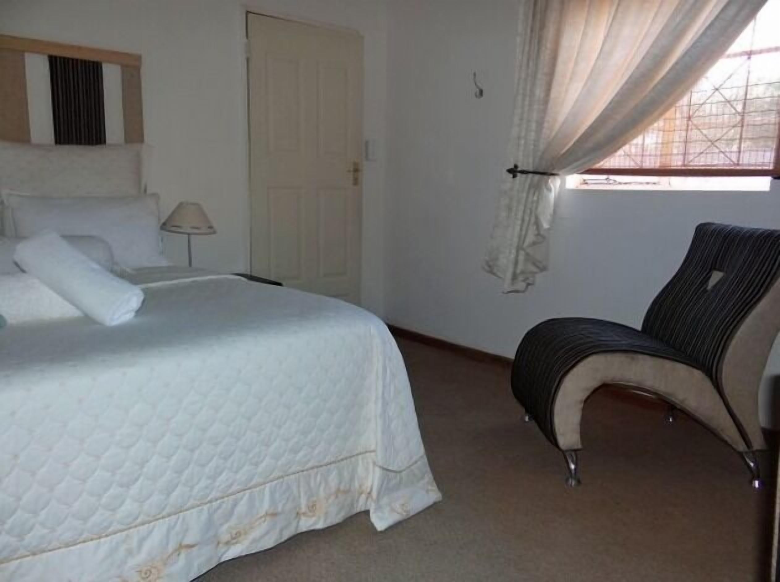 Een slaapkamer met een bed, een stoel, een deur en een raam met gordijnen.