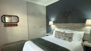Ein Schlafzimmer mit einem Bett, einem Deckenventilator, einem Nachttisch, einer Lampe, einer Kommode und einem an der Wand befestigten Spiegel.