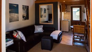 Ein gemütliches Wohnzimmer mit einer schwarzen Couch, einem kleinen Tisch und einem Spiegel. Eine Treppe führt zu einer oberen Ebene.