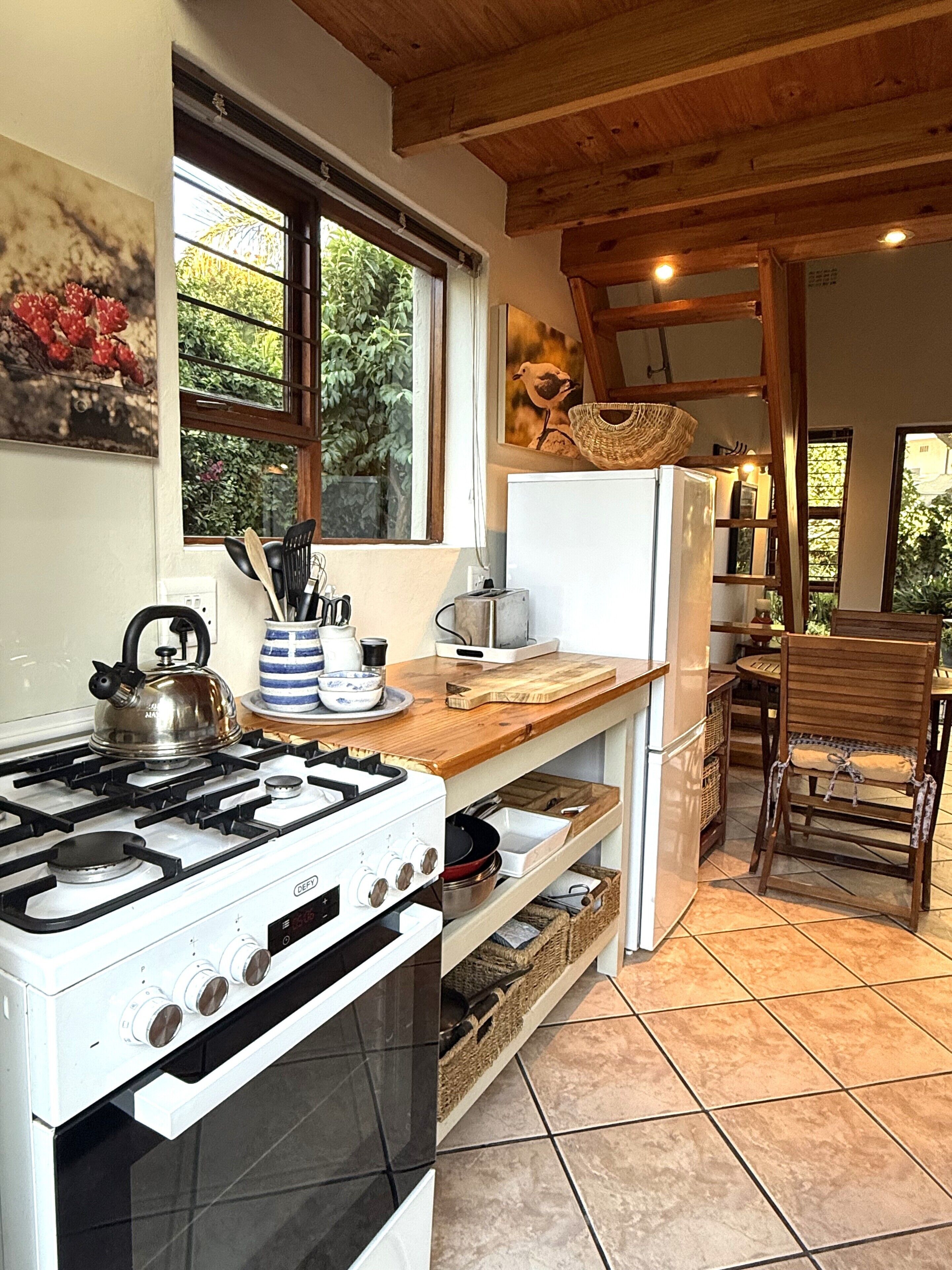 A kitchen with a stove, refrigerator, wooden counter, and a dining area with a chair.