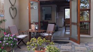 Eine offene Terrasse mit Korbstühlen, einem Tisch mit Flasche und Glas sowie Blumentöpfen.