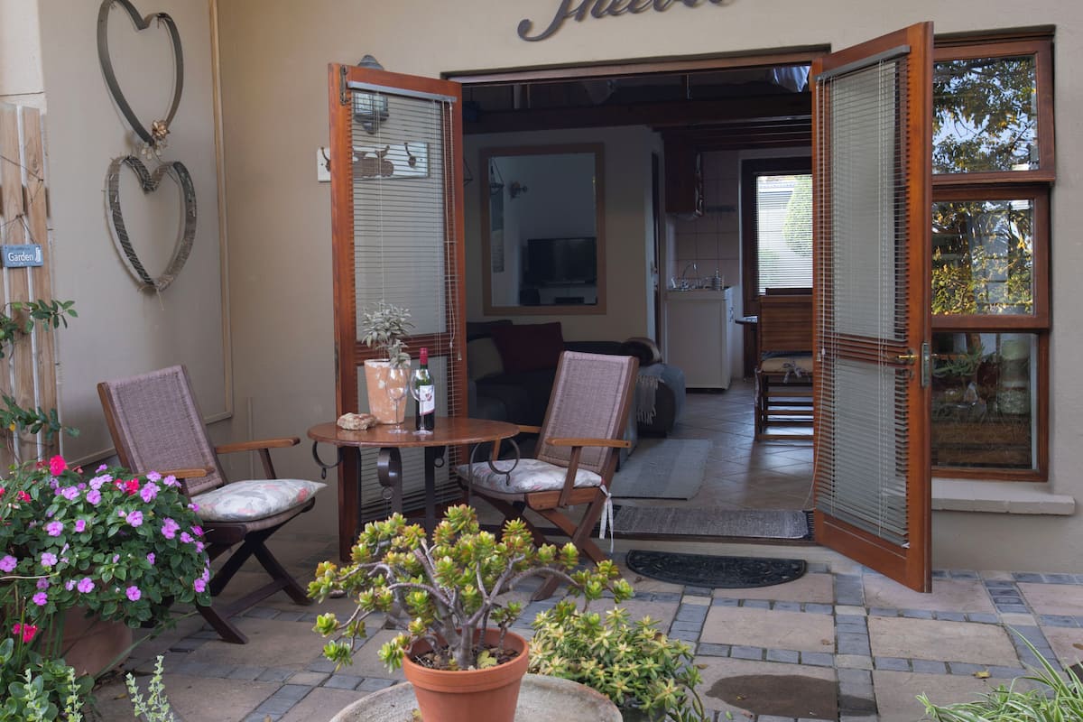 Un patio abierto con sillas de mimbre, una mesa con una botella y un vaso, y plantas en macetas.
