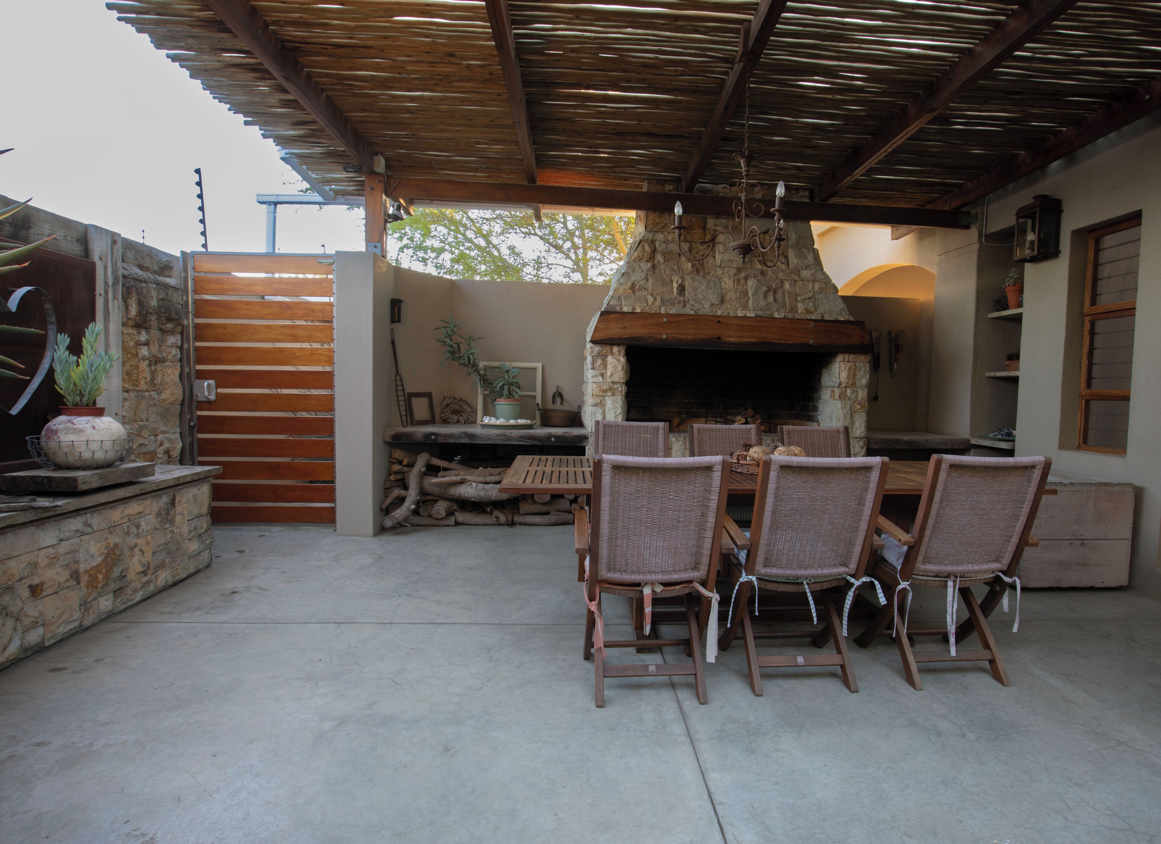 An outdoor patio with a stone fireplace, wicker chairs, and a wooden table.