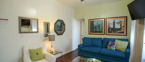 A living room with a white armchair, a blue sofa, a glass coffee table, and a ceiling fan.