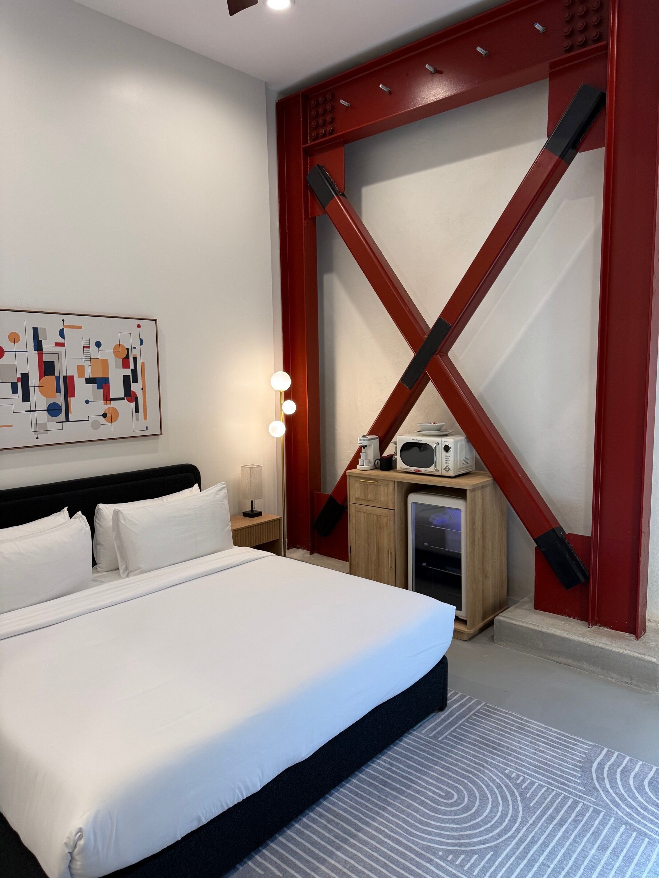 Habitació d'hotel amb un llit gran, una taula de nit amb microones, una làmpada i una obra d'art penjada a la paret.