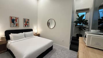 Une chambre d’hôtel moderne équipée d’un lit, d’une table de chevet, d’une lampe, d’une œuvre d’art, d’un miroir, d’une plante en pot et d’un four à micro-ondes.