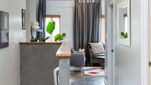 A modern kitchen with a grey countertop, a wooden bench, and a grey sofa. There is a plant on the counter and a colorful rug on the floor. - Hotel Royal (Long Beach)