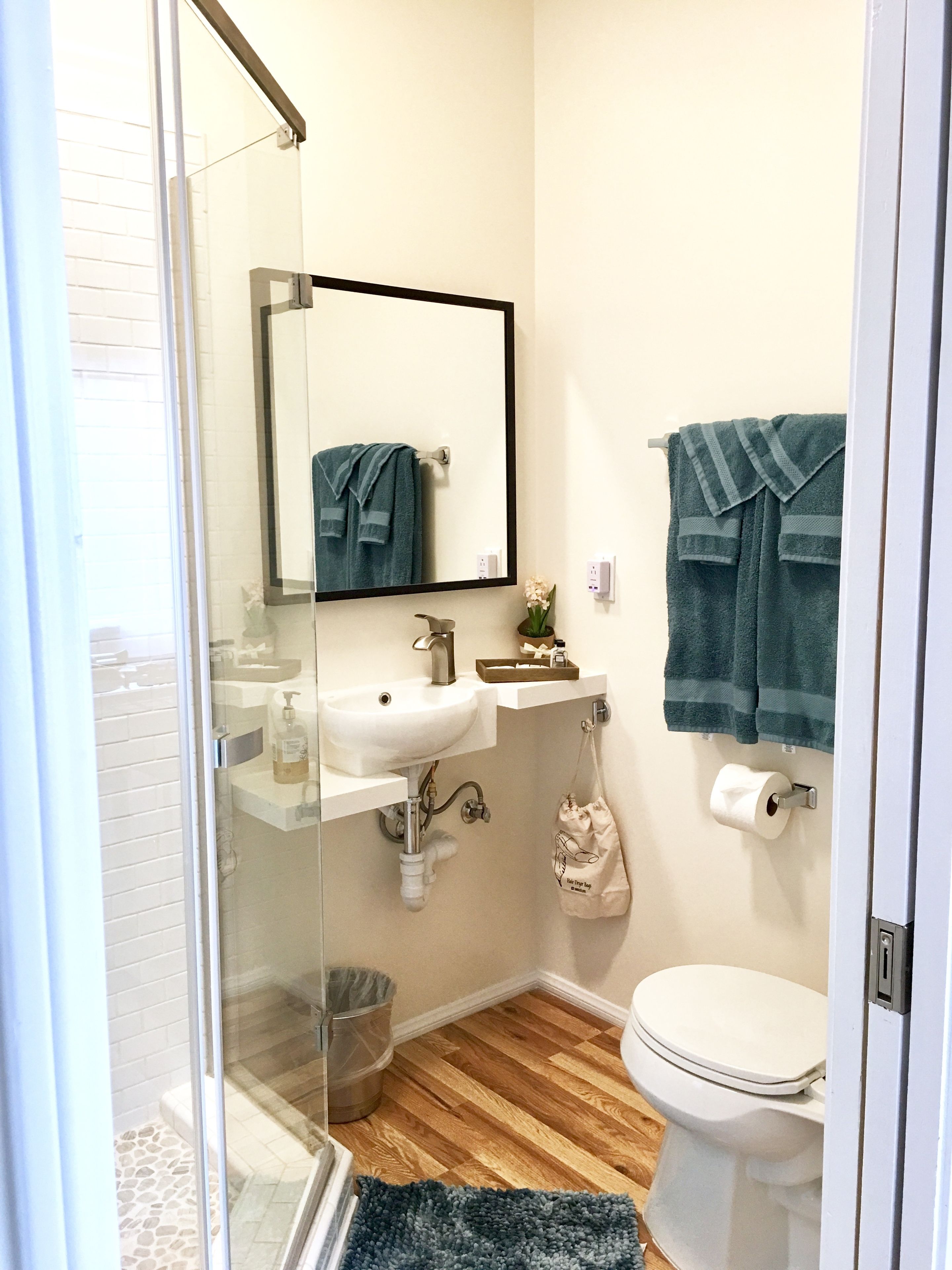 Un baño con cabina de ducha de vidrio, un lavabo blanco con espejo encima, un inodoro y una alfombra azul en el suelo.
