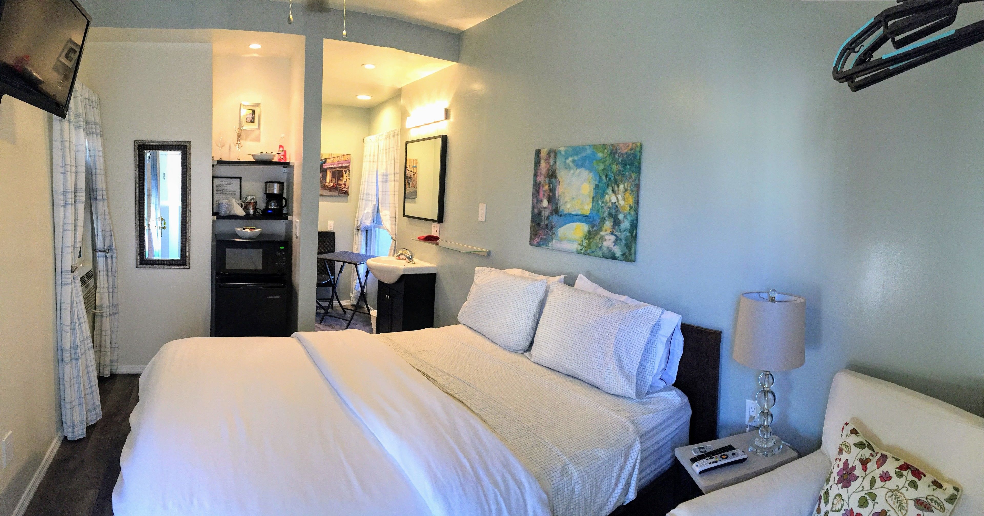 Une chambre d’hôtel avec un grand lit, un bureau avec une chaise, une machine à café et un tableau au mur.