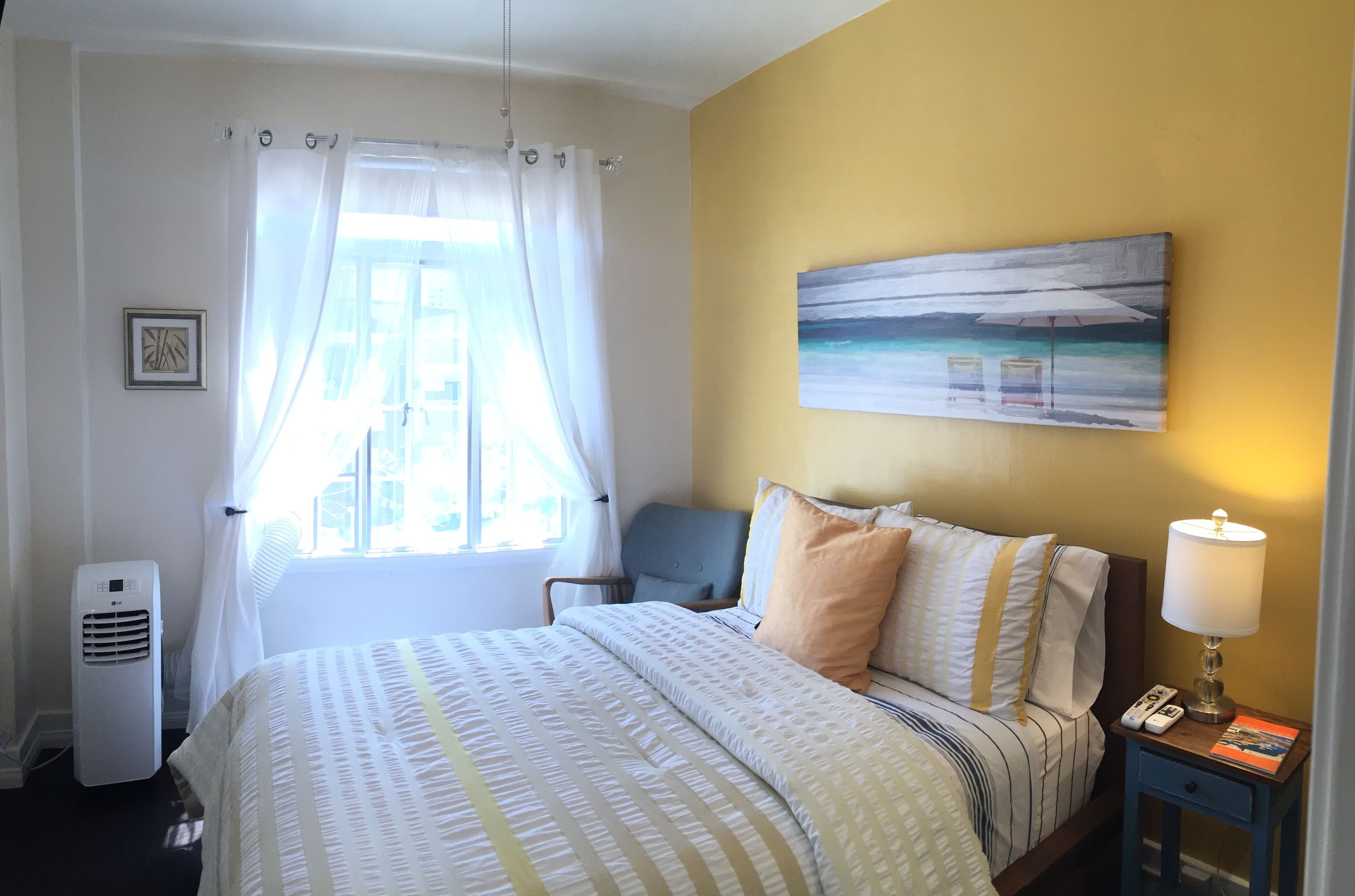 A hotel room with a bed, a chair, a painting on the wall, a lamp, and a window with curtains.
