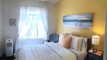 Una habitación de hotel con cama, una silla, un cuadro en la pared, una lámpara y una ventana con cortinas.